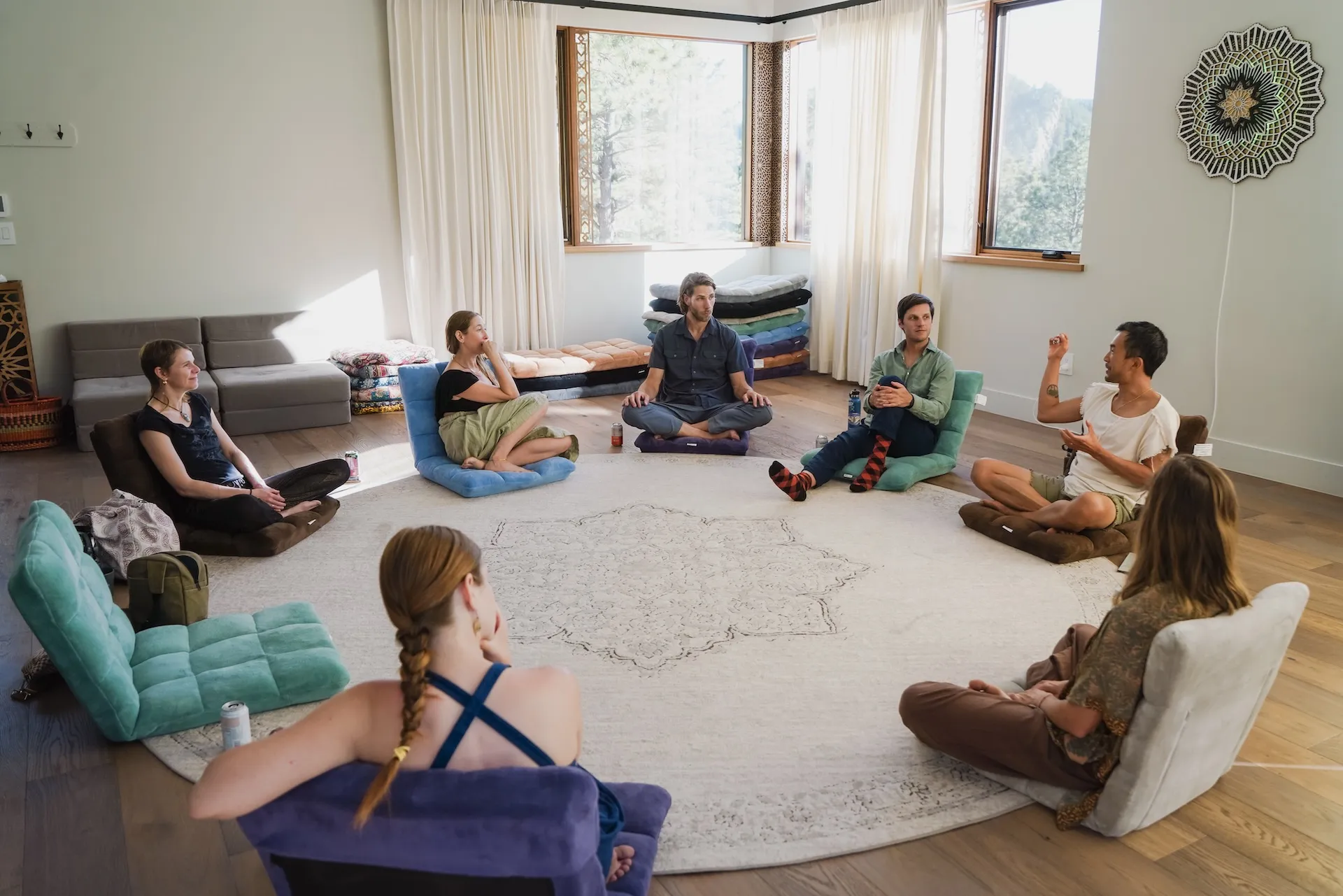 Participants sitting together in a circle on floor cushions in a sunlit North Boulder room